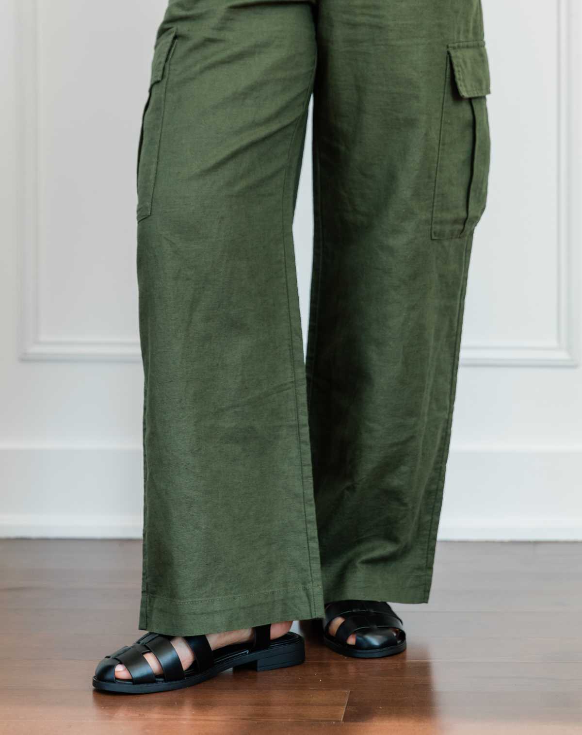 Cropped view of woman's legs wearing black fisherman sandals with full length wide olive green linen pants.