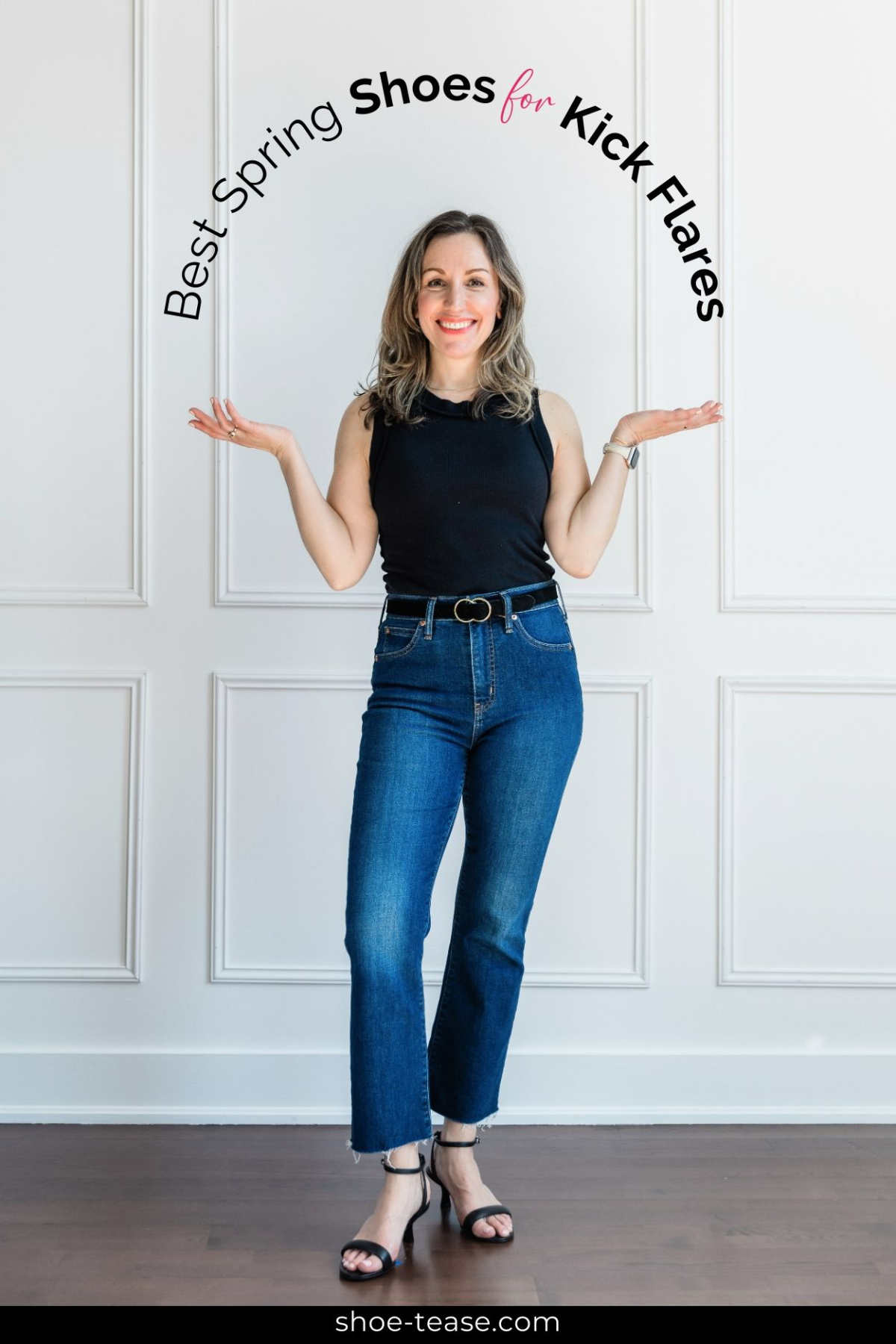 Woman wearing a black tank top, blue denim kick flares with black belt and sandals standing in front of a white wall with overlay words reading best spring shoes for kick flares. 