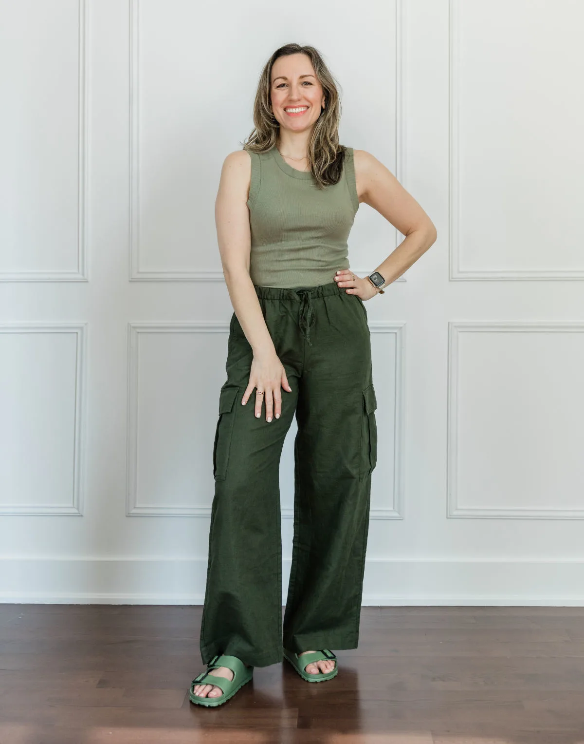 Woman wearing a light green tank top, olive green linen pants and green Birkenstock style sandals.