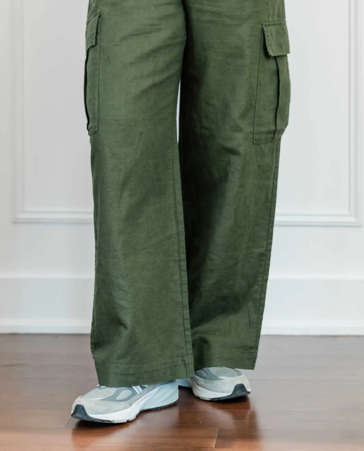 Cropped view of woman's legs wearing grey New Balance dad sneakers with full length wide olive green linen pants.