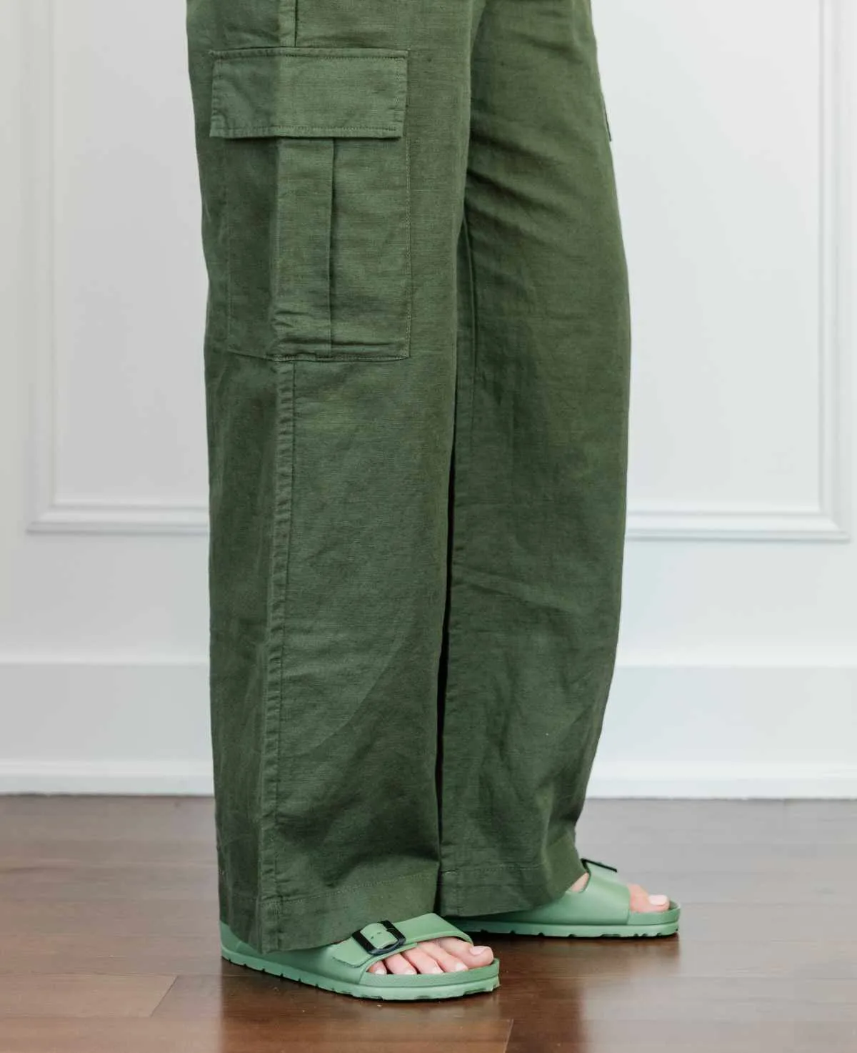 Cropped view of woman's legs wearing green Birkenstock like sandals with full length wide olive green linen pants.