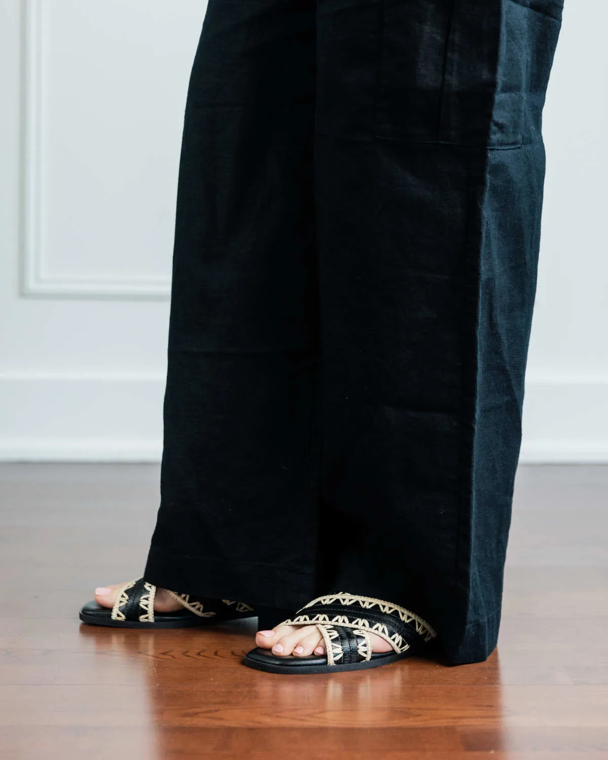 Cropped view of woman's legs wearing black and tan slide sandals with full length wide leg black linen pants.