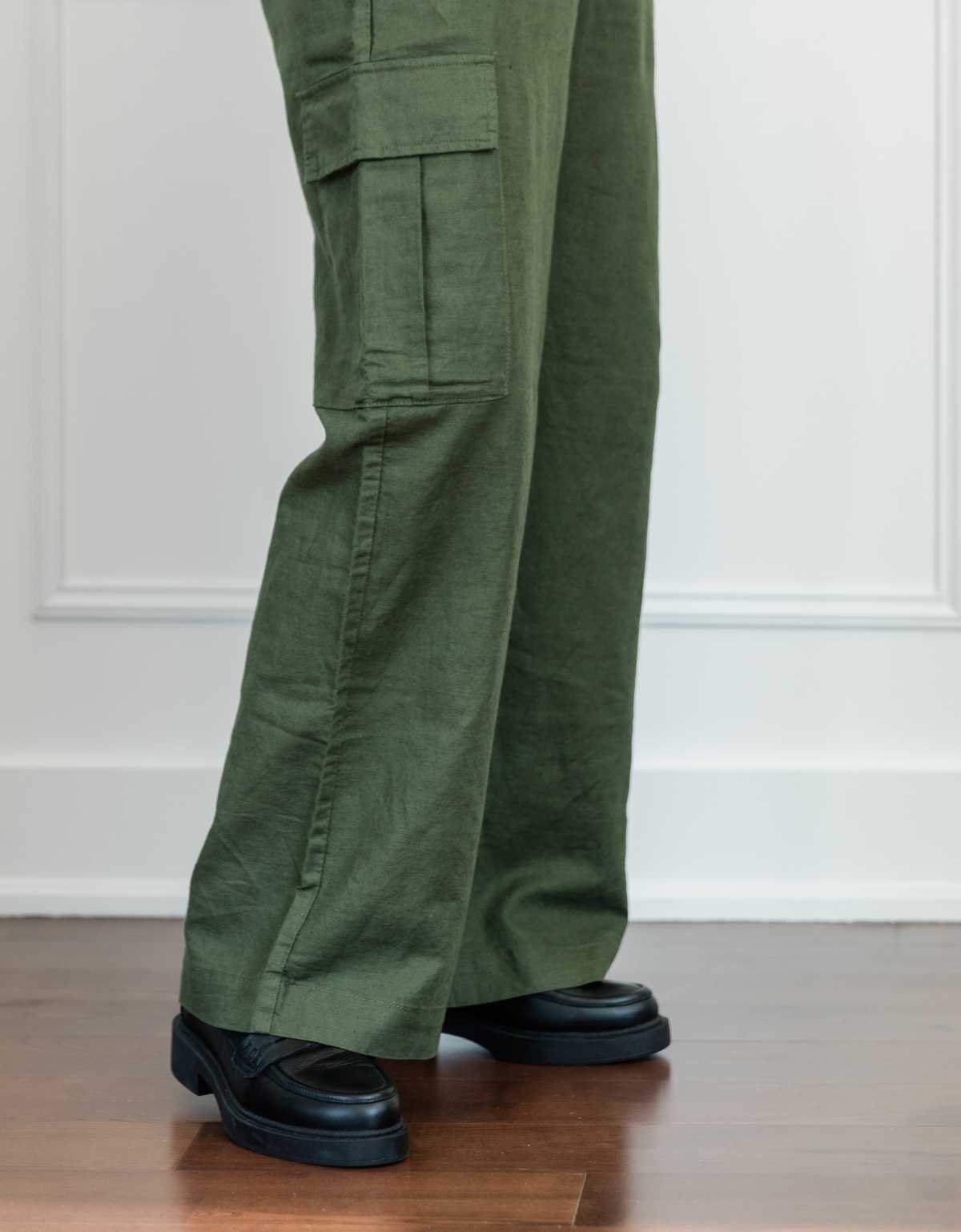 Cropped view of woman's legs wearing black chunky loafers with full length wide olive green linen pants.
