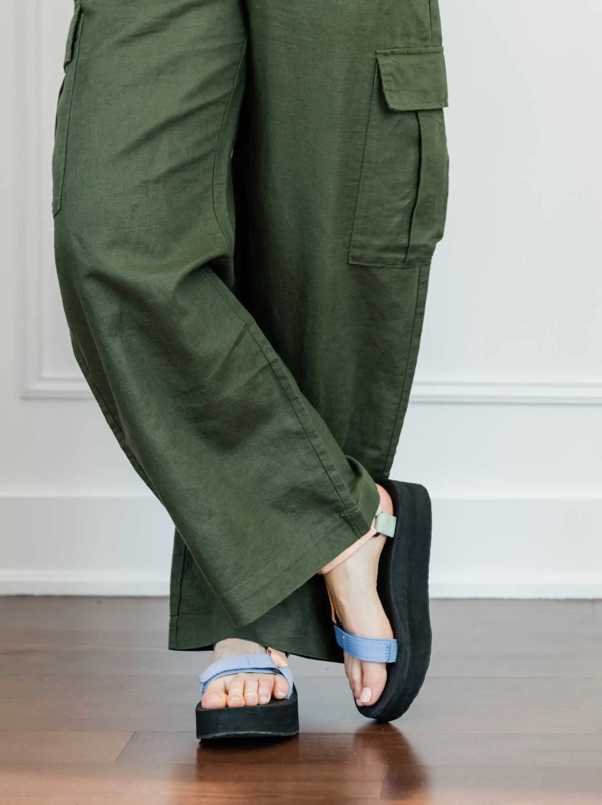 Cropped view of woman's legs wearing colorful platform Teva sandals with full length wide olive green linen pants.