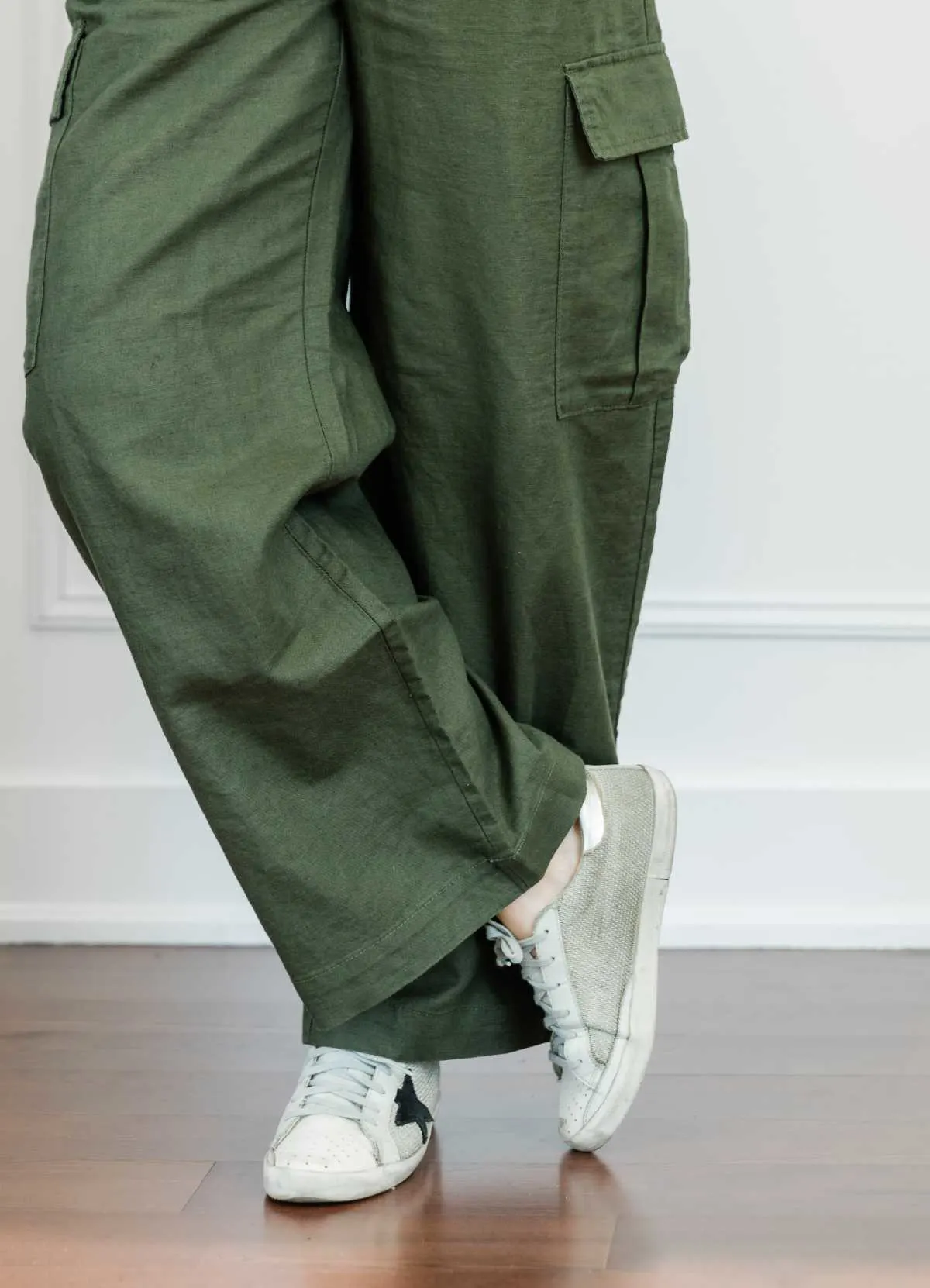 Cropped view of woman's legs wearing sleek off white star sneakers with full length wide olive green linen pants.