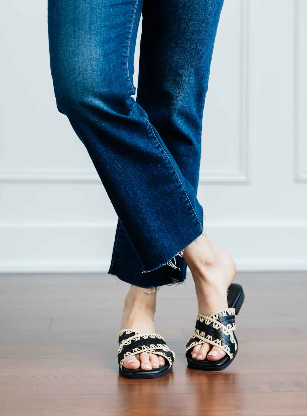 Cropped view of woman's legs wearing black criss cross low slides with raffia detail and kick flares.
