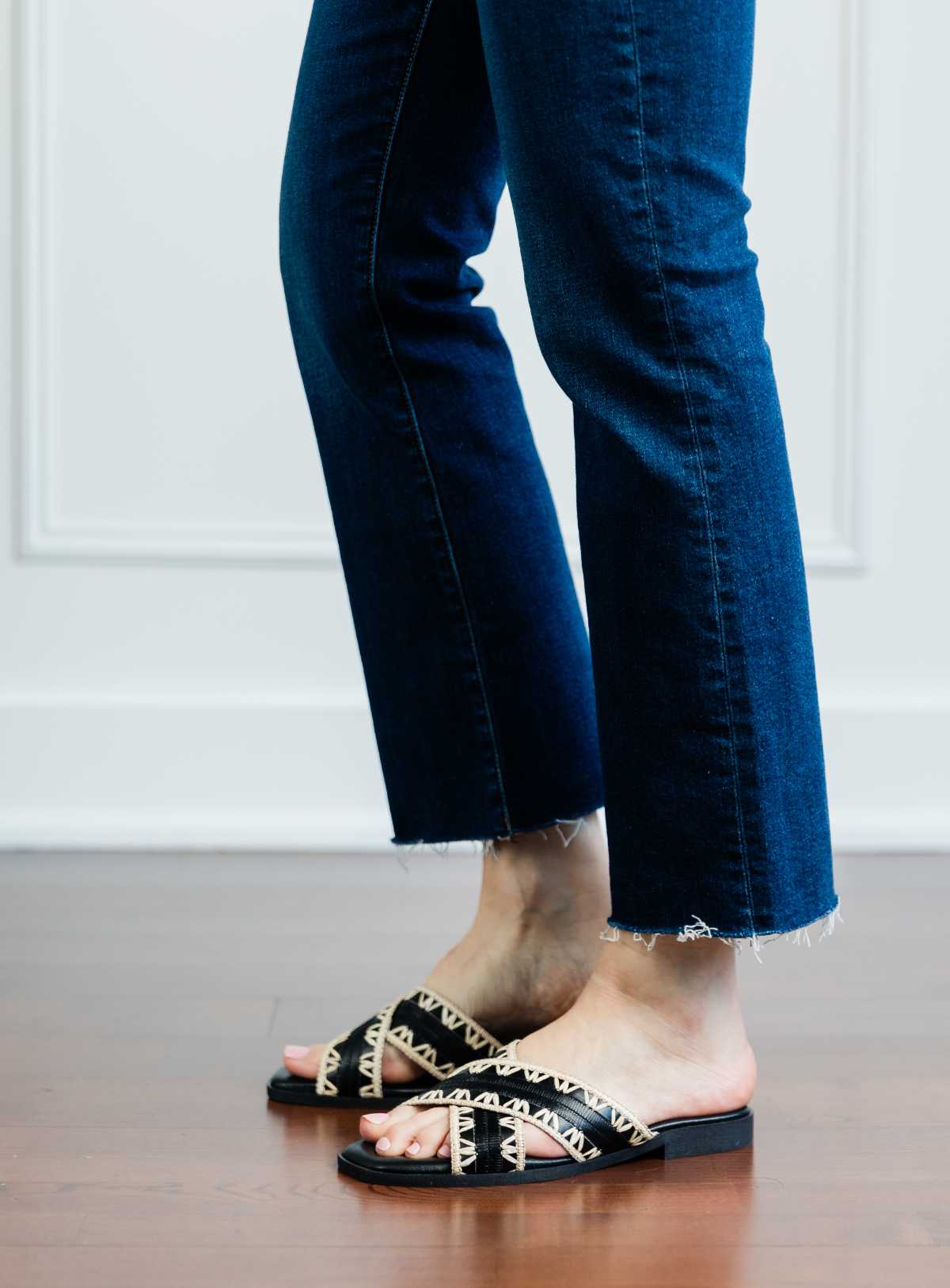 Cropped view of woman's legs wearing black criss cross low slides with raffia detail and kick flares.