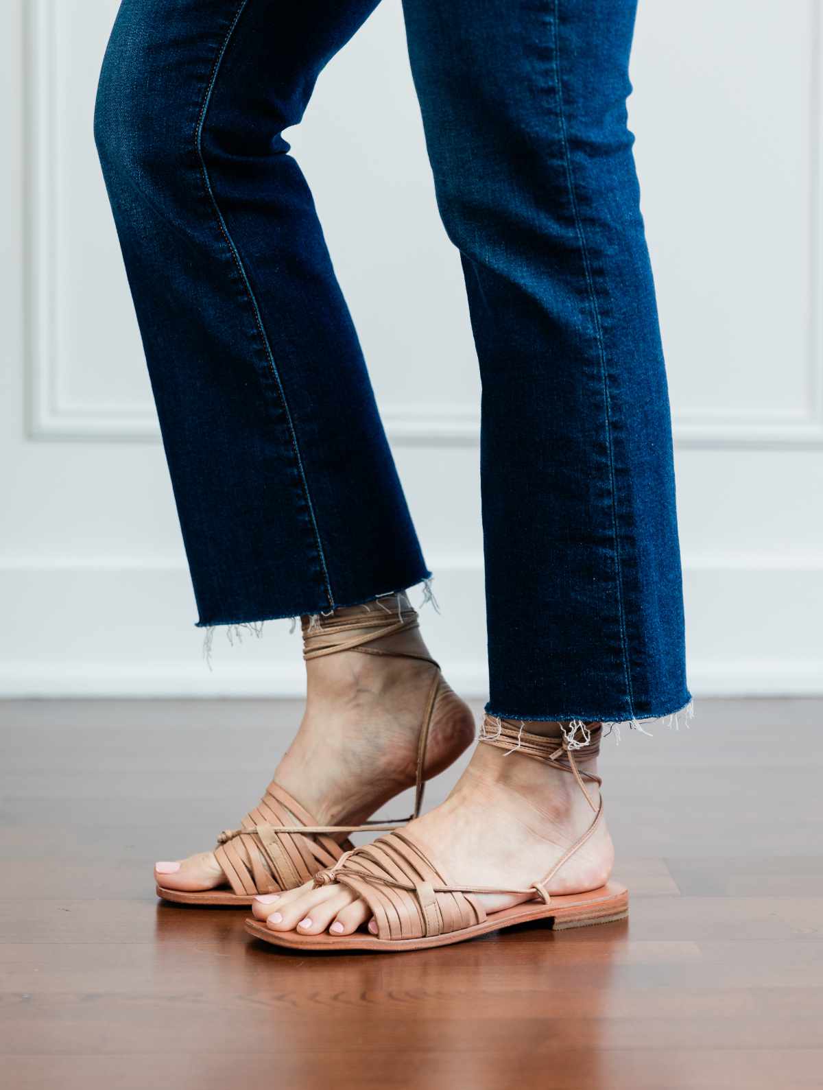 Cropped view of woman's legs wearing beige strappy green style sandals with kick flares.