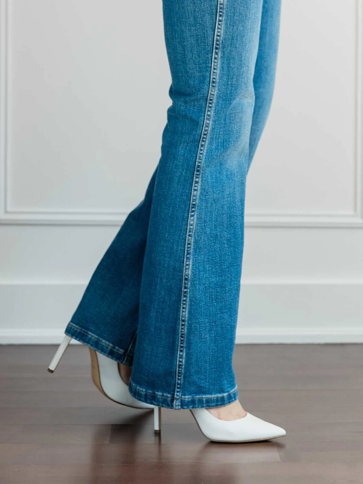 Cropped view of woman's legs wearing  white pumps with full length blue flare jeans.