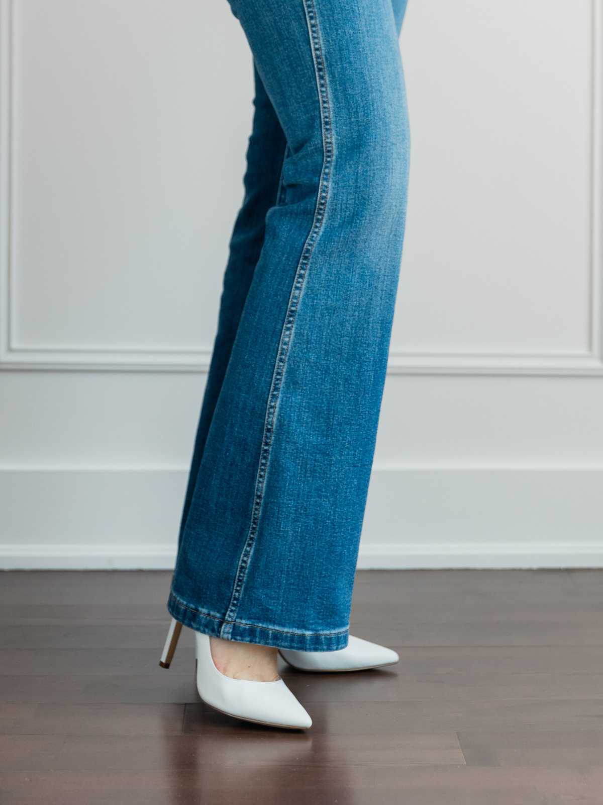 Cropped view of woman's legs wearing  white pumps with full length blue flare jeans.