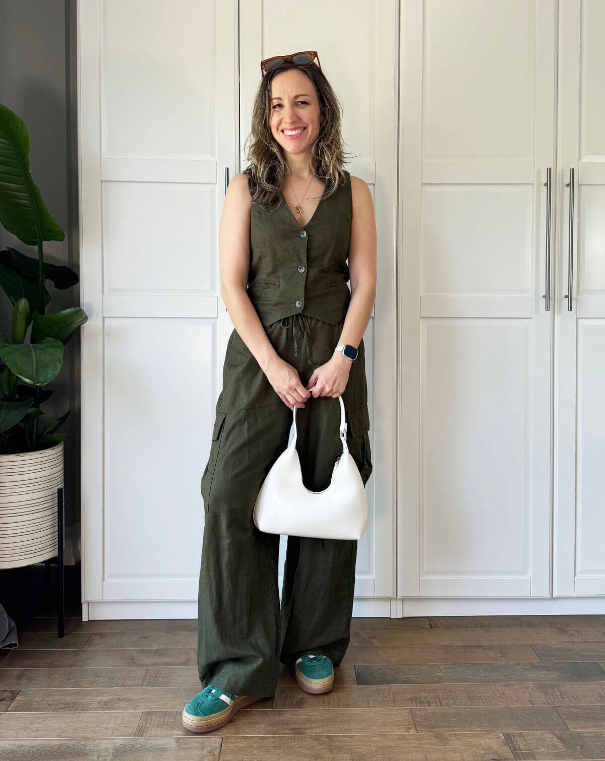 Woman posing wearing olive green matching set with long pants, green platform sneakers and white purse.