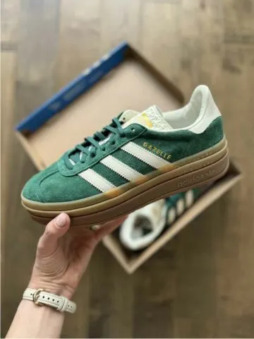 CLose up of woman's hand holding a green adidas sneaker over an open shoe box.