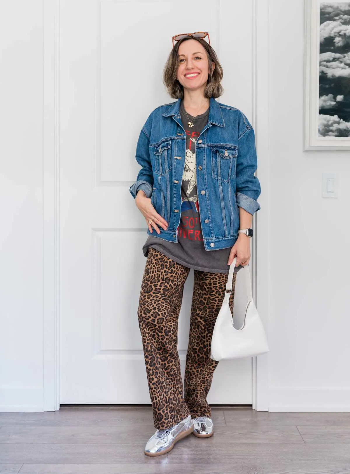 Woman posing in silver sneakers, cheetah pants, graphic tee and denim jacket.